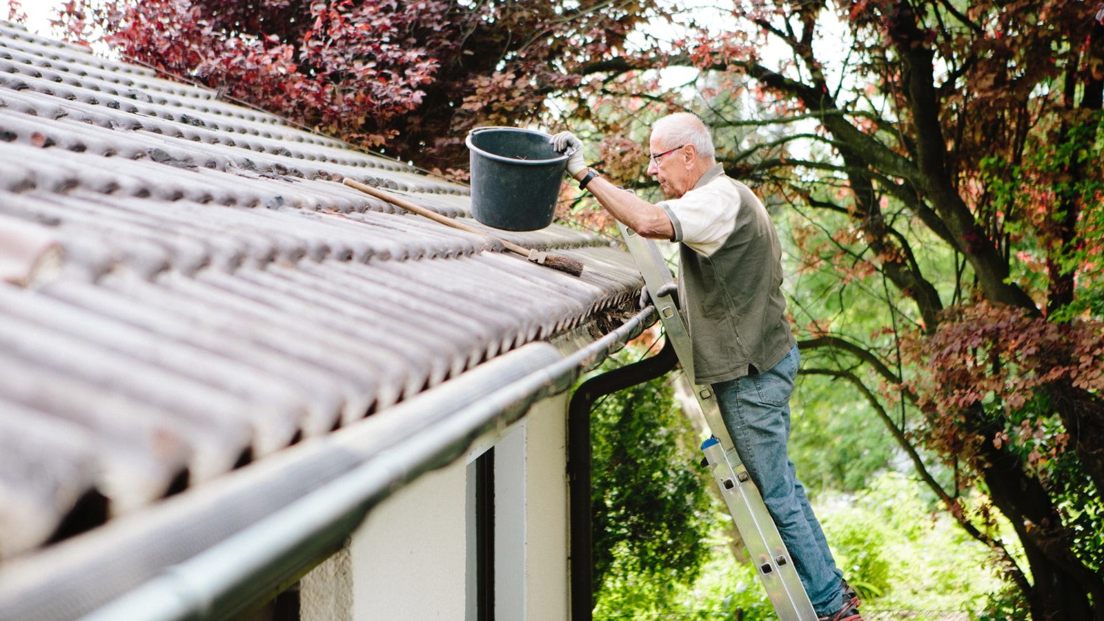Older man cleaning rain gutters on his house